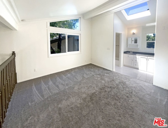 unfurnished living room featuring lofted ceiling with skylight, ornamental molding, sink, and dark carpet