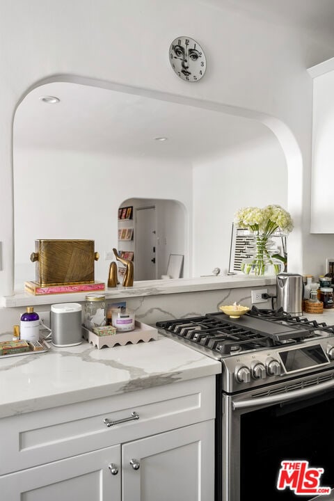 kitchen with white cabinets, light stone counters, and stainless steel range with gas cooktop