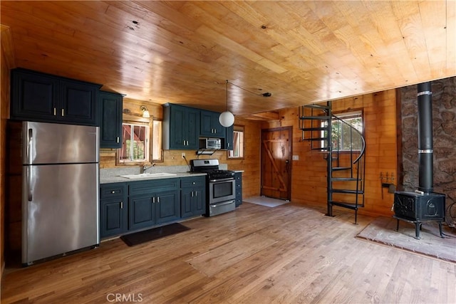 kitchen with wooden walls, wooden ceiling, stainless steel appliances, a wood stove, and sink