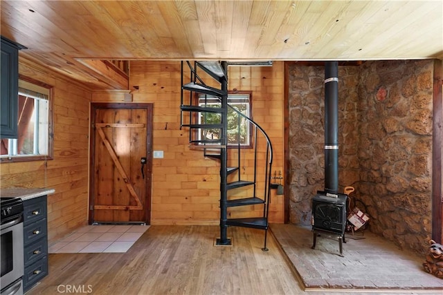 interior space with wood walls, a wood stove, light hardwood / wood-style floors, and wooden ceiling