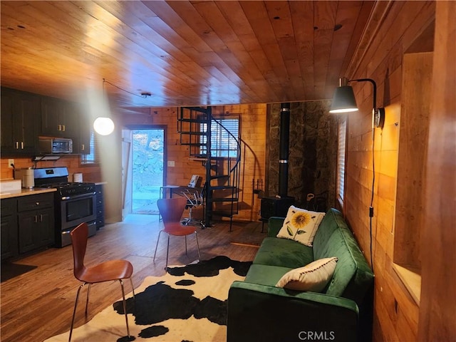 living room featuring wood ceiling, a wood stove, light hardwood / wood-style flooring, and wooden walls