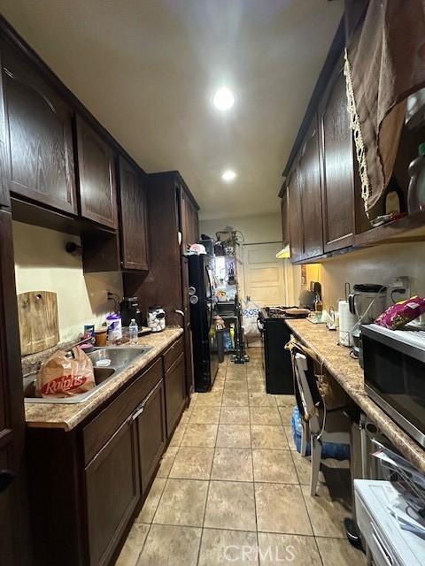 kitchen featuring dark brown cabinets, light tile patterned flooring, and black fridge