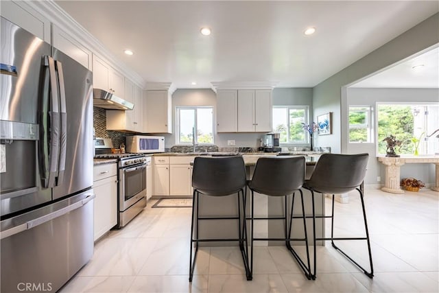 kitchen with a breakfast bar area, appliances with stainless steel finishes, backsplash, stone countertops, and white cabinets