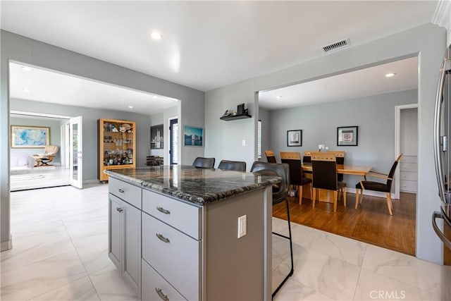 kitchen with a kitchen breakfast bar, dark stone countertops, gray cabinets, and a kitchen island