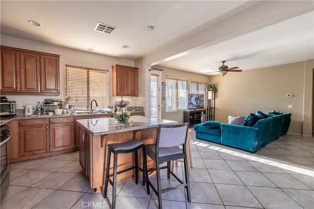 kitchen featuring ceiling fan, light tile patterned flooring, sink, a center island, and a kitchen bar