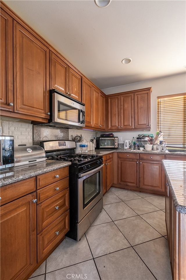 kitchen with appliances with stainless steel finishes, light tile patterned floors, and backsplash