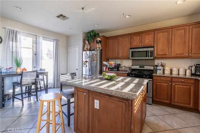 kitchen with a kitchen island, light stone counters, decorative backsplash, stainless steel appliances, and light tile patterned flooring