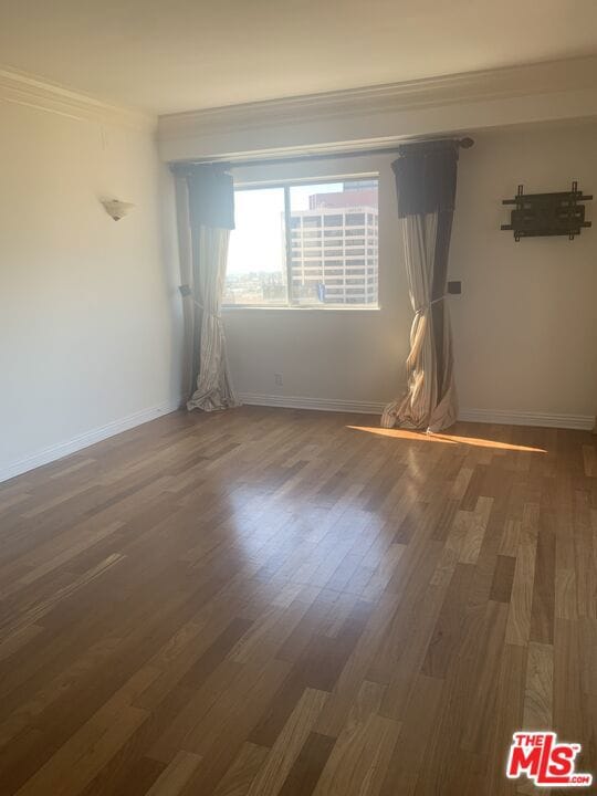 empty room with dark hardwood / wood-style flooring and crown molding