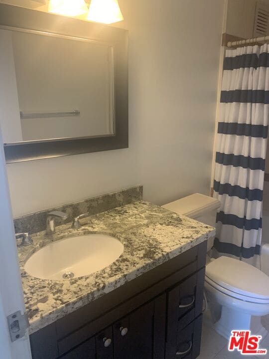 bathroom with tile patterned flooring, vanity, toilet, and curtained shower