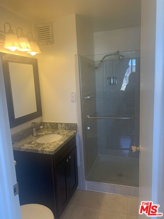 bathroom featuring tile patterned floors, vanity, toilet, and a shower with door