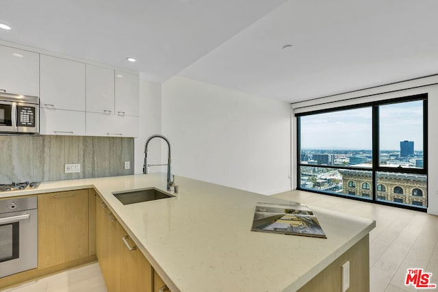 kitchen with white cabinetry, sink, light stone counters, kitchen peninsula, and appliances with stainless steel finishes