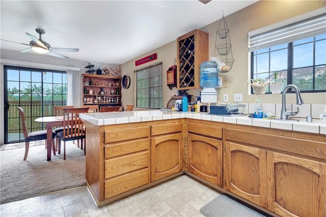 kitchen with tile countertops, light carpet, sink, ceiling fan, and kitchen peninsula