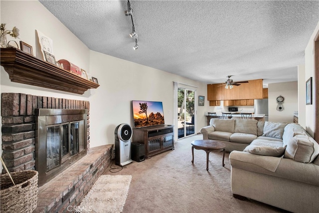 living room with ceiling fan, a brick fireplace, a textured ceiling, track lighting, and light carpet