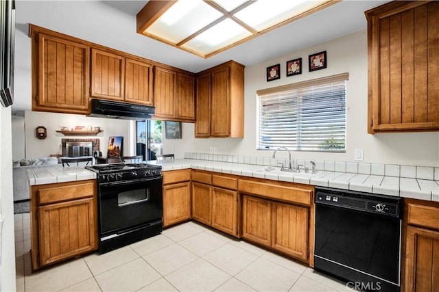 kitchen with sink, kitchen peninsula, black appliances, tile countertops, and a fireplace