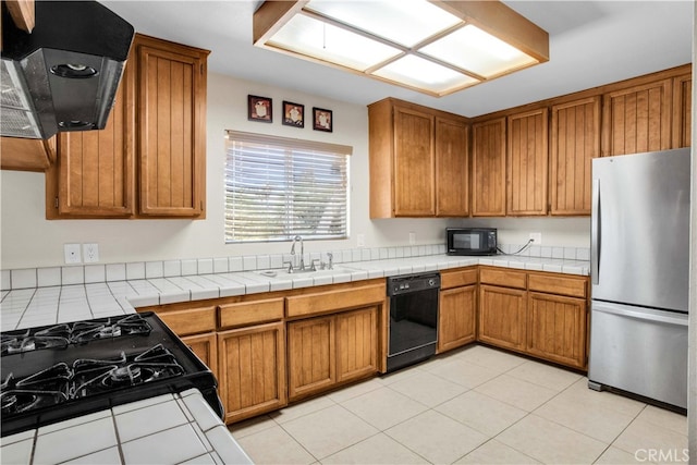 kitchen with light tile patterned floors, sink, extractor fan, black appliances, and tile counters