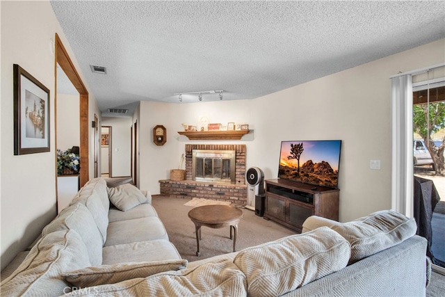 carpeted living room with a textured ceiling, track lighting, and a brick fireplace