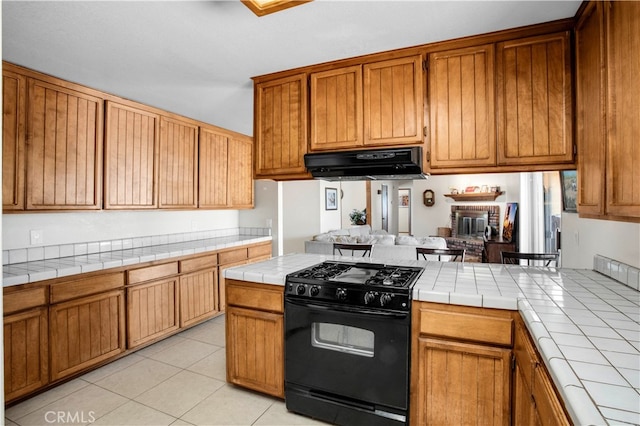 kitchen featuring black gas stove, a fireplace, light tile patterned flooring, and tile countertops