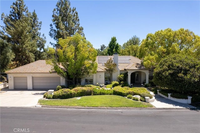 view of front of property with a garage, a front lawn, and solar panels