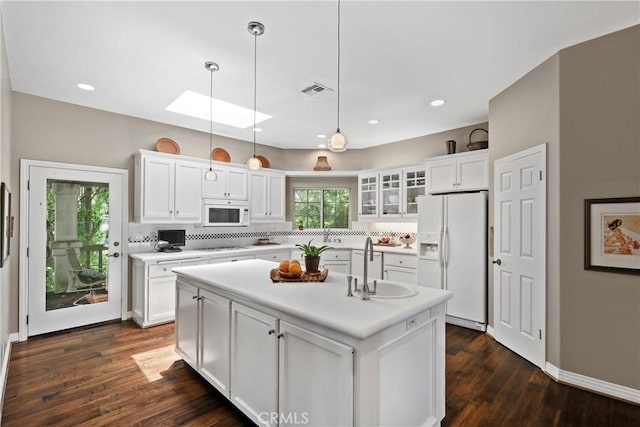 kitchen featuring white cabinetry, a center island with sink, white appliances, and a skylight