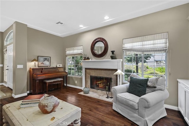 sitting room with a tiled fireplace, dark wood-type flooring, and plenty of natural light