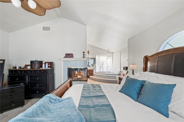 bedroom featuring a tiled fireplace, light carpet, ceiling fan, and lofted ceiling with beams