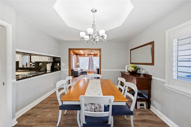 dining space with a chandelier, a tray ceiling, and dark wood-type flooring