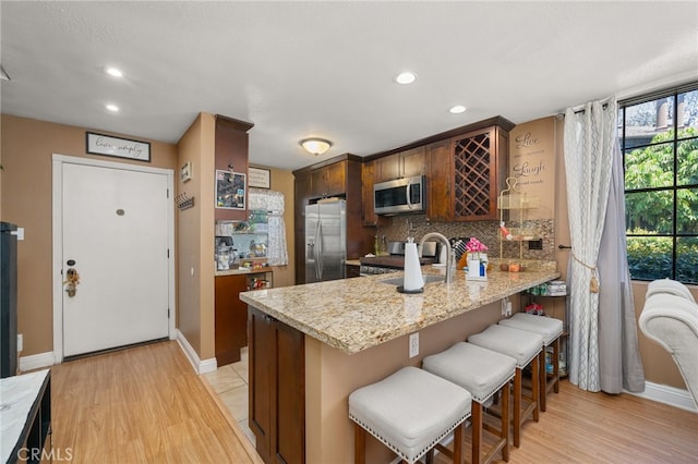 kitchen featuring sink, kitchen peninsula, light hardwood / wood-style flooring, stainless steel appliances, and a kitchen breakfast bar