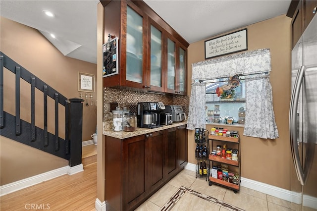 kitchen with stainless steel fridge, decorative backsplash, dark brown cabinets, and light tile patterned floors