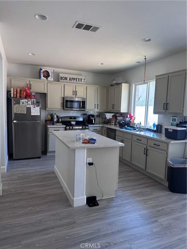 kitchen featuring appliances with stainless steel finishes, a kitchen island, hardwood / wood-style floors, and tasteful backsplash