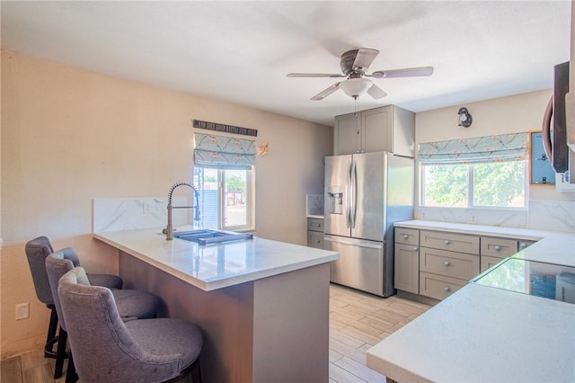 kitchen with light countertops, a sink, stainless steel refrigerator with ice dispenser, a breakfast bar area, and gray cabinets