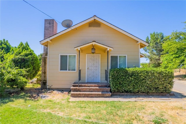 bungalow-style home featuring a chimney and a front lawn