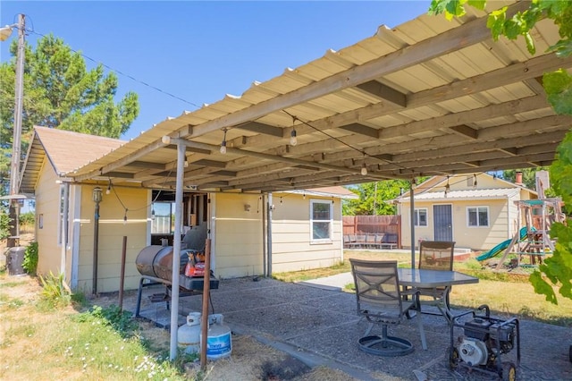 view of patio with an attached carport, an outbuilding, an exterior structure, and a playground