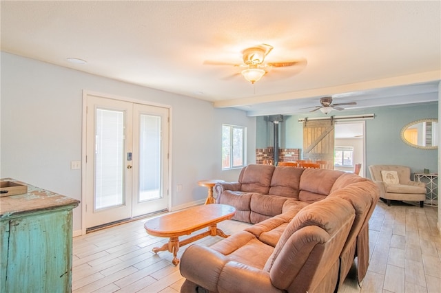 living room featuring light hardwood / wood-style floors, a barn door, beamed ceiling, ceiling fan, and french doors