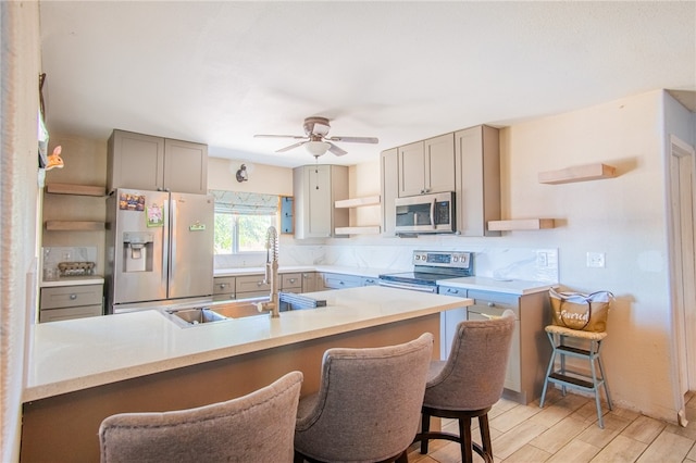 kitchen featuring ceiling fan, sink, appliances with stainless steel finishes, a breakfast bar, and light wood-type flooring