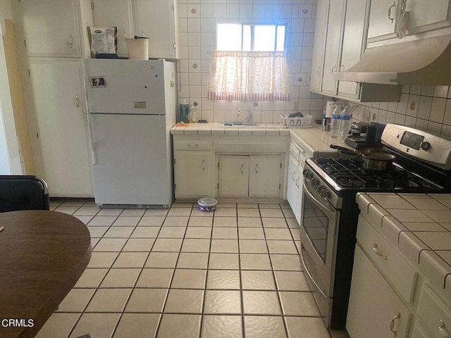 kitchen with tile countertops, sink, stainless steel range with gas stovetop, white fridge, and tasteful backsplash