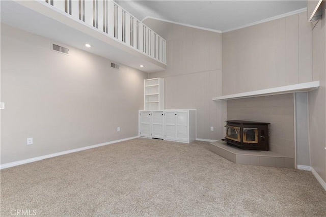 unfurnished living room featuring a wood stove, carpet floors, and ornamental molding