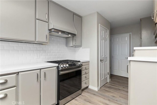 kitchen with premium range hood, backsplash, gray cabinets, stainless steel range with gas stovetop, and light wood-type flooring