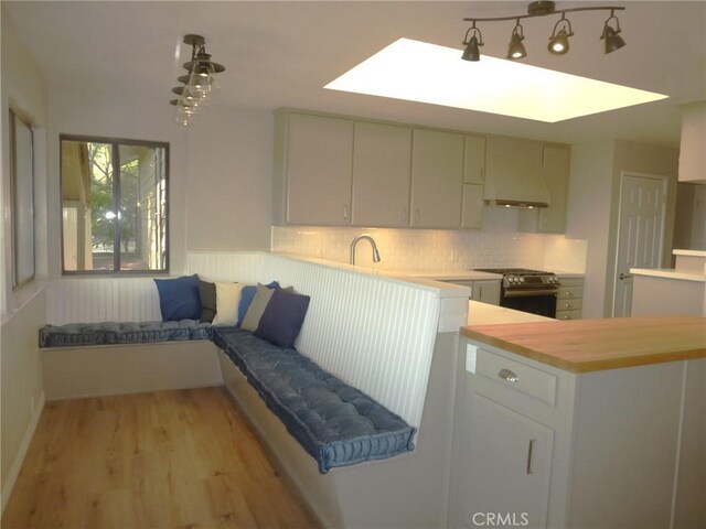 kitchen featuring white cabinetry, wooden counters, stainless steel range oven, light hardwood / wood-style floors, and custom range hood