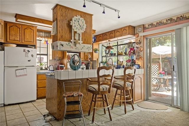 kitchen with a breakfast bar area, white fridge, tile countertops, and kitchen peninsula