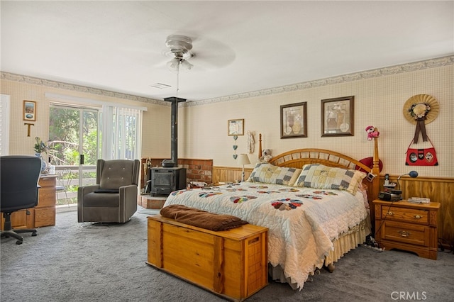 carpeted bedroom with ceiling fan, wood walls, and a wood stove