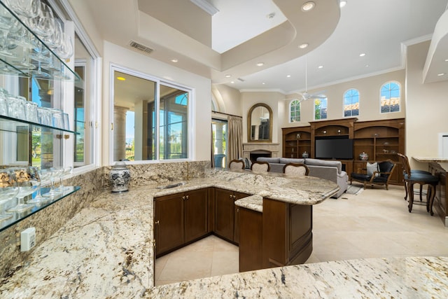 kitchen with light tile patterned floors, ornamental molding, light stone countertops, and kitchen peninsula