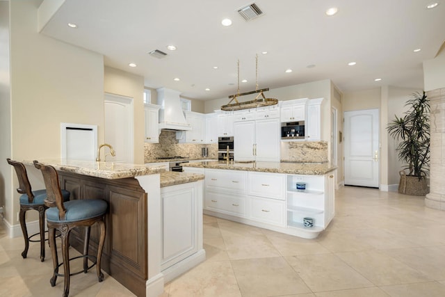 kitchen with premium range hood, backsplash, white cabinetry, a spacious island, and light stone countertops