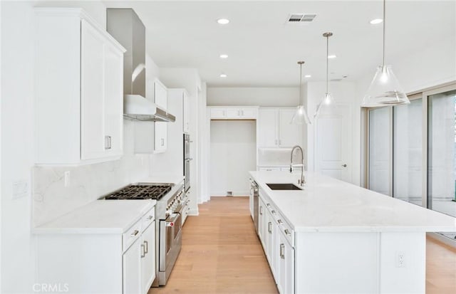 kitchen with white cabinets, appliances with stainless steel finishes, a center island with sink, and hanging light fixtures