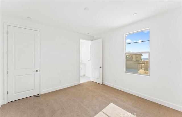 unfurnished bedroom with ensuite bathroom and light carpet