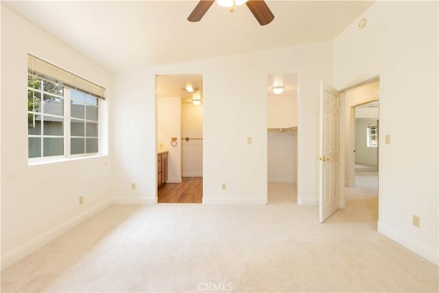 unfurnished bedroom featuring lofted ceiling, connected bathroom, a walk in closet, light colored carpet, and ceiling fan