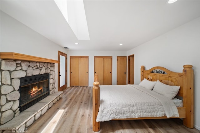 bedroom with light hardwood / wood-style floors, a fireplace, a skylight, and multiple closets