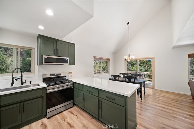 kitchen with kitchen peninsula, green cabinetry, light hardwood / wood-style flooring, appliances with stainless steel finishes, and an inviting chandelier