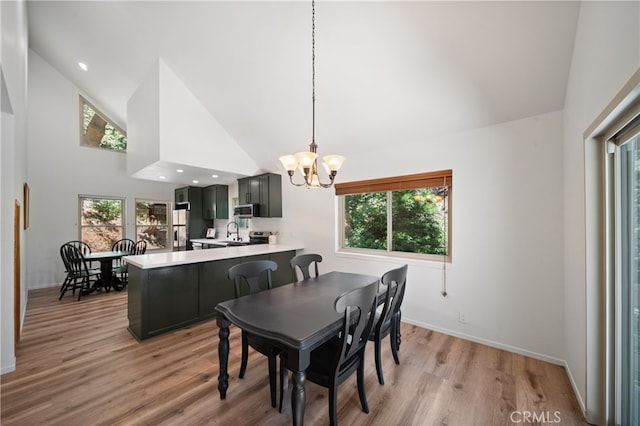 dining space with a notable chandelier, light hardwood / wood-style flooring, sink, and high vaulted ceiling