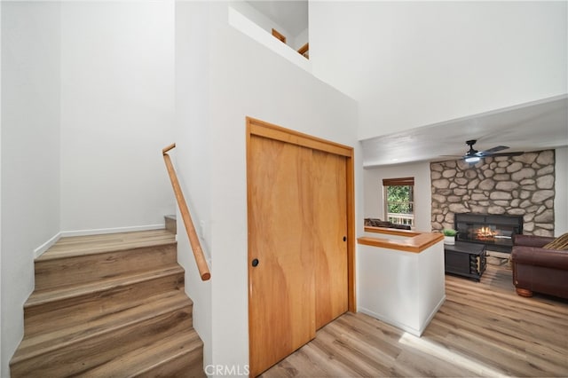 stairs featuring a towering ceiling, ceiling fan, hardwood / wood-style flooring, and a fireplace