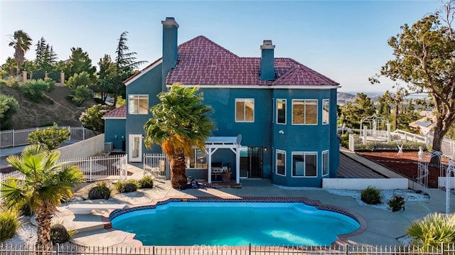 rear view of property featuring a fenced in pool and a patio